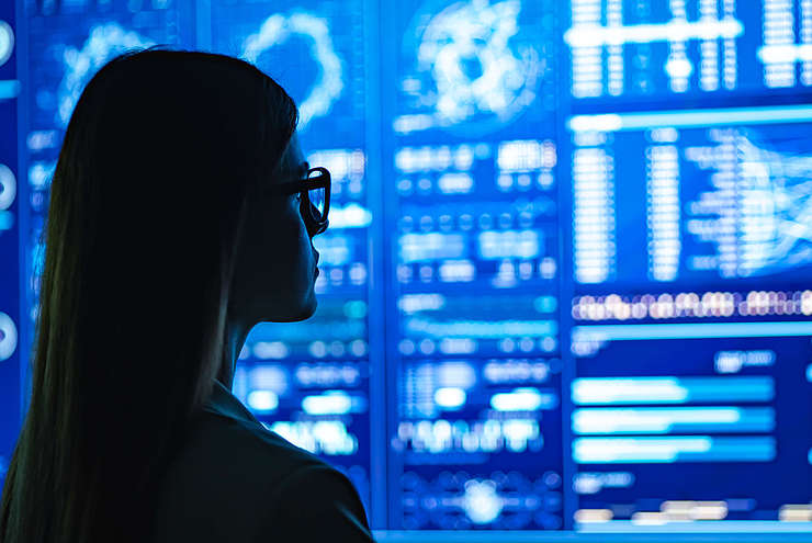 Image showing a woman looking a wall of monitors. Monitors show different kinds of data visualization.